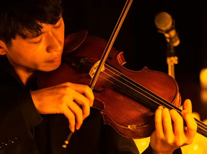 Man playing the violin around candles